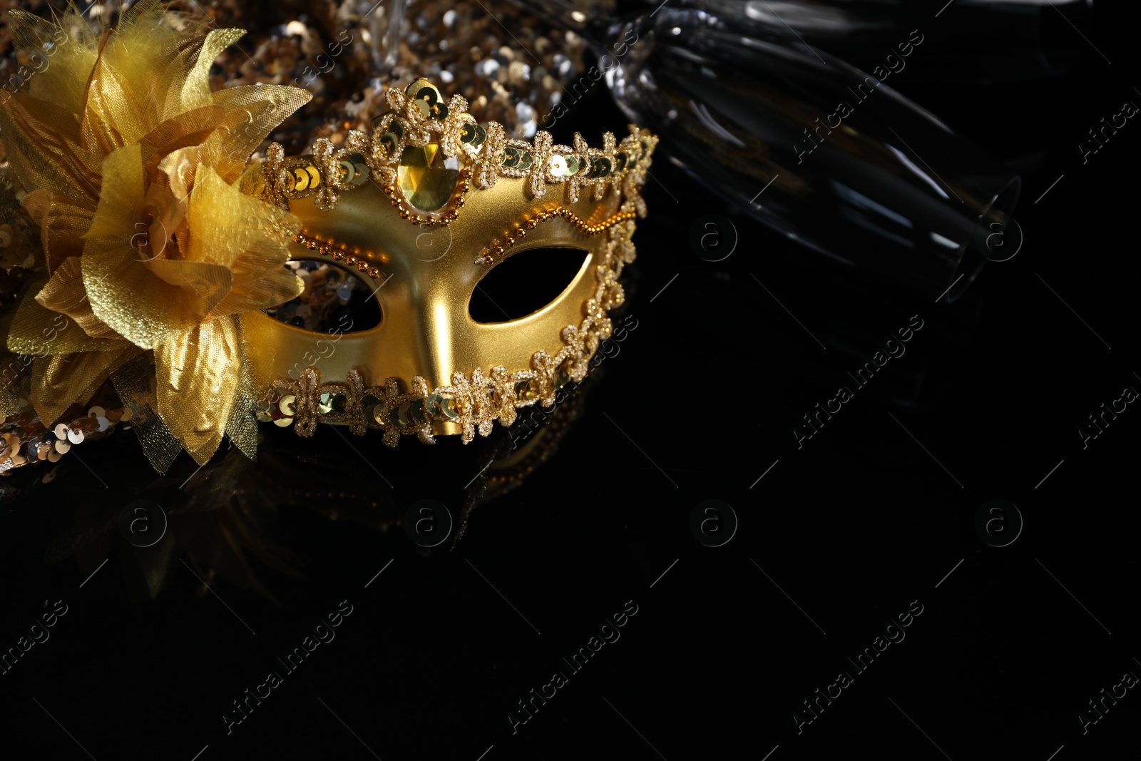 Photo of Beautiful golden carnival mask and champagne glass on black background, closeup. Space for text