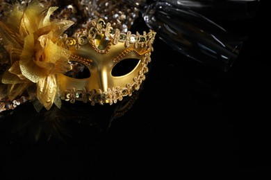 Photo of Beautiful golden carnival mask and champagne glass on black background, closeup. Space for text