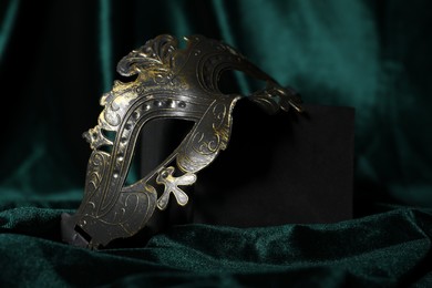 Photo of Beautiful carnival mask on green fabric, closeup