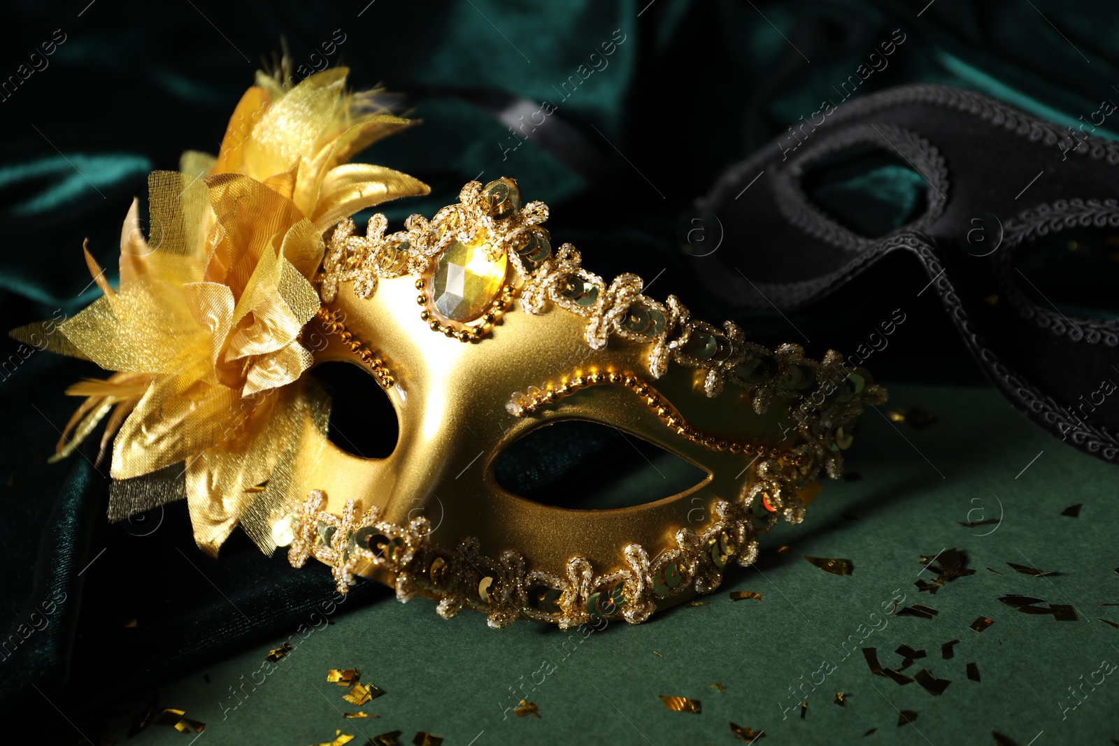 Photo of Beautiful golden carnival masks and silk fabric on green background, closeup