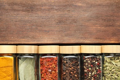 Photo of Different spices in glass jars on wooden table, top view. Space for text