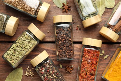 Photo of Different spices in glass jars on wooden table, flat lay