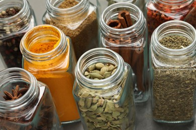 Photo of Different spices in glass jars on grey table, closeup