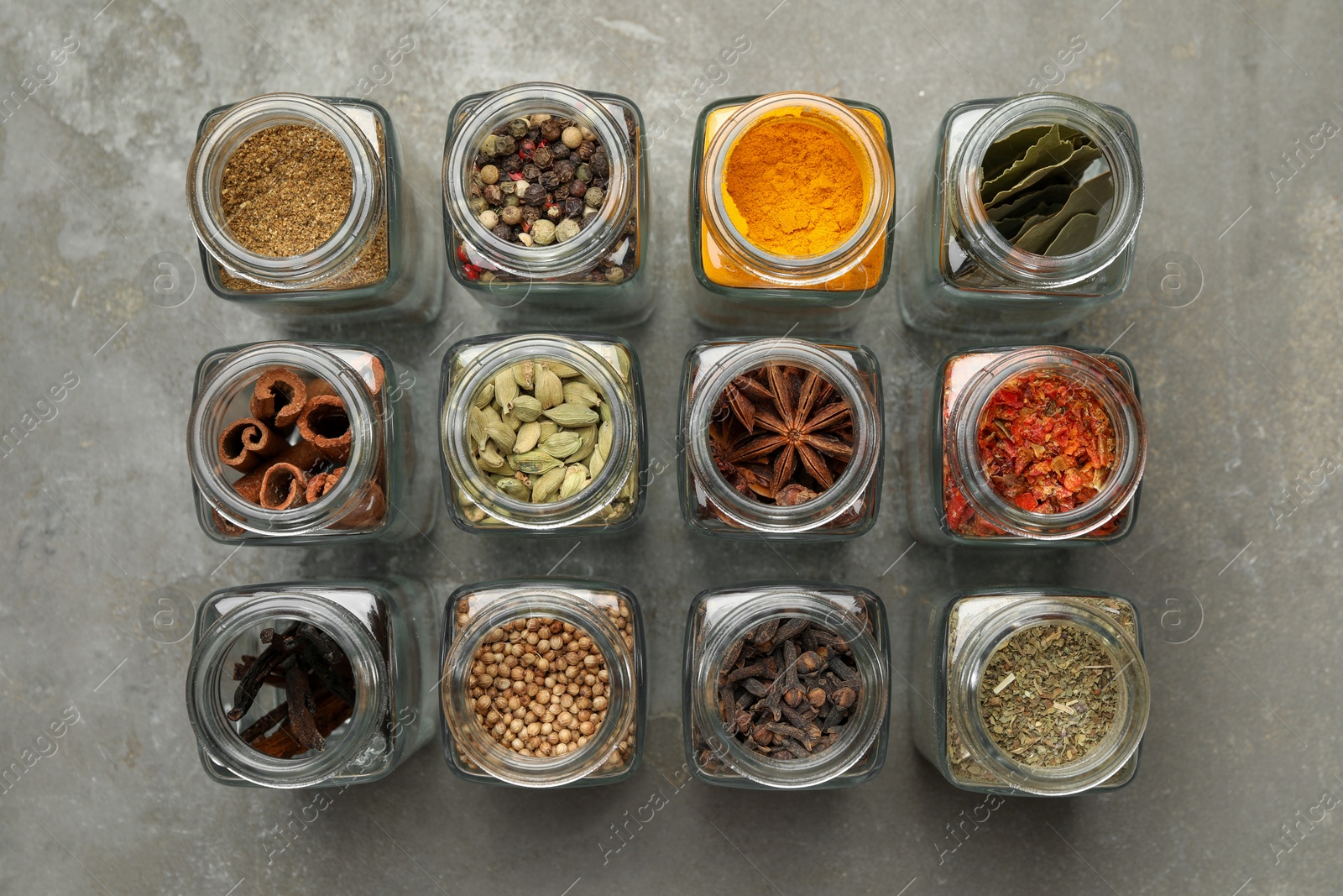 Photo of Different spices in glass jars on grey table, flat lay