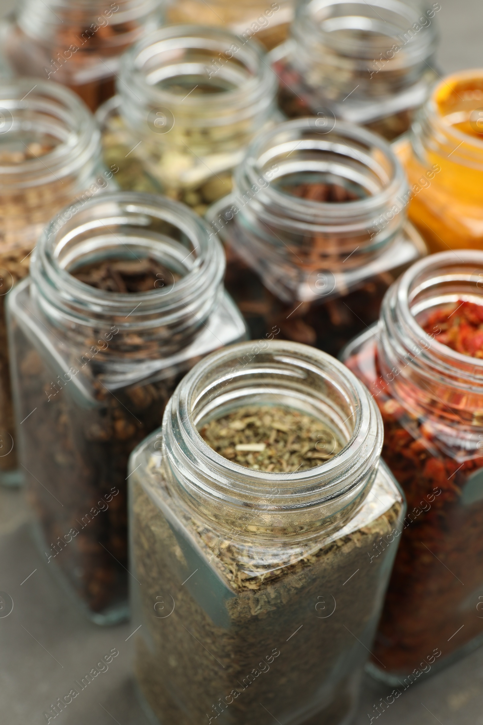 Photo of Different spices in glass jars on grey table, closeup