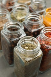 Different spices in glass jars on grey table, closeup