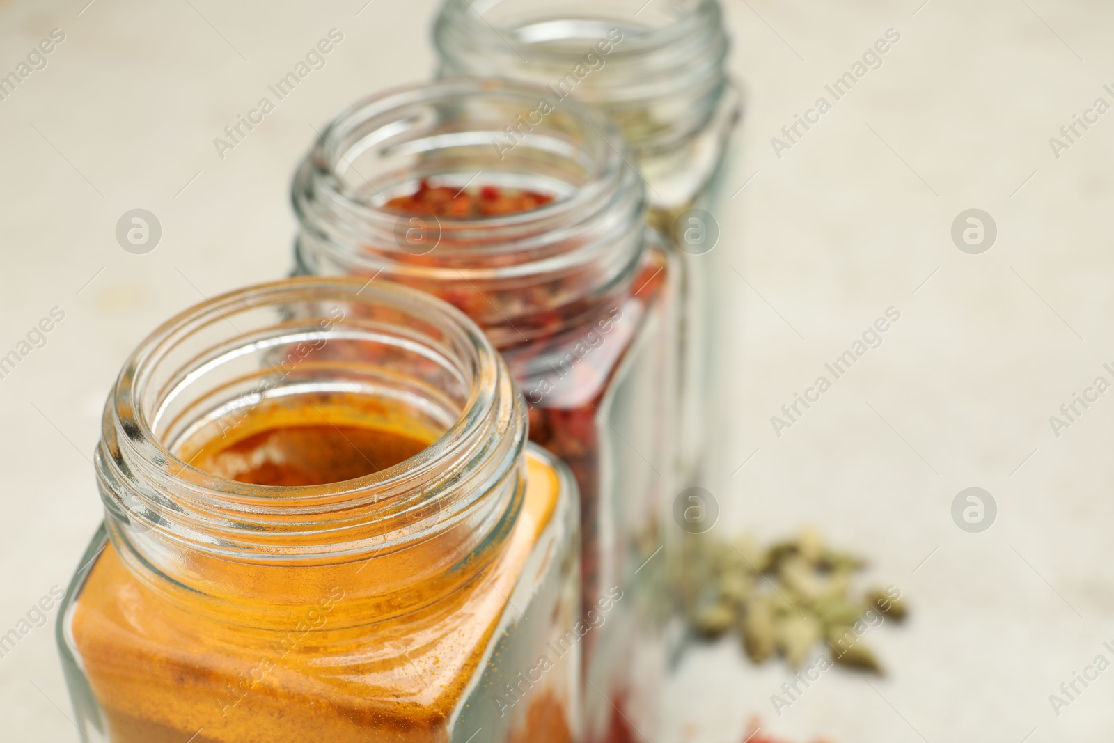 Photo of Different spices in glass jars on light grey table, closeup. Space for text