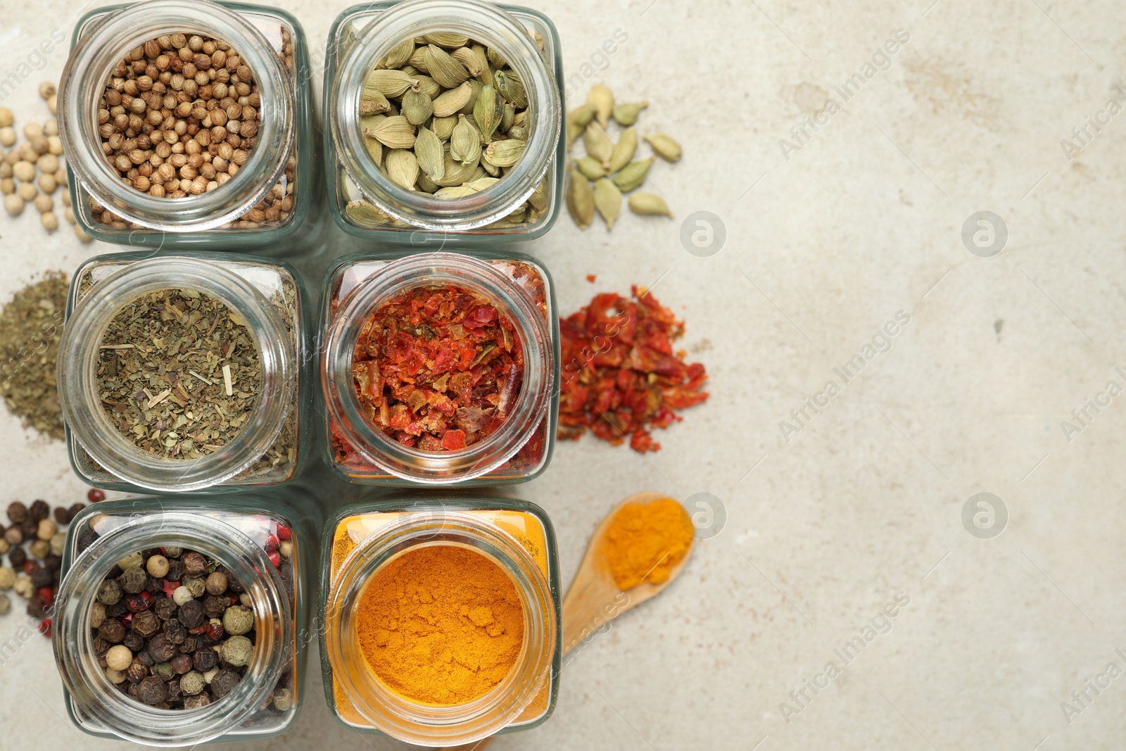 Photo of Different spices in glass jars on light grey table, top view. Space for text