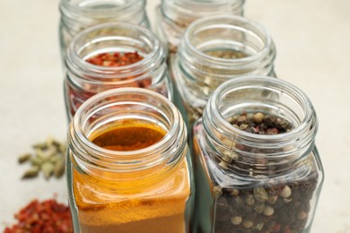 Different spices in glass jars on light grey table, closeup