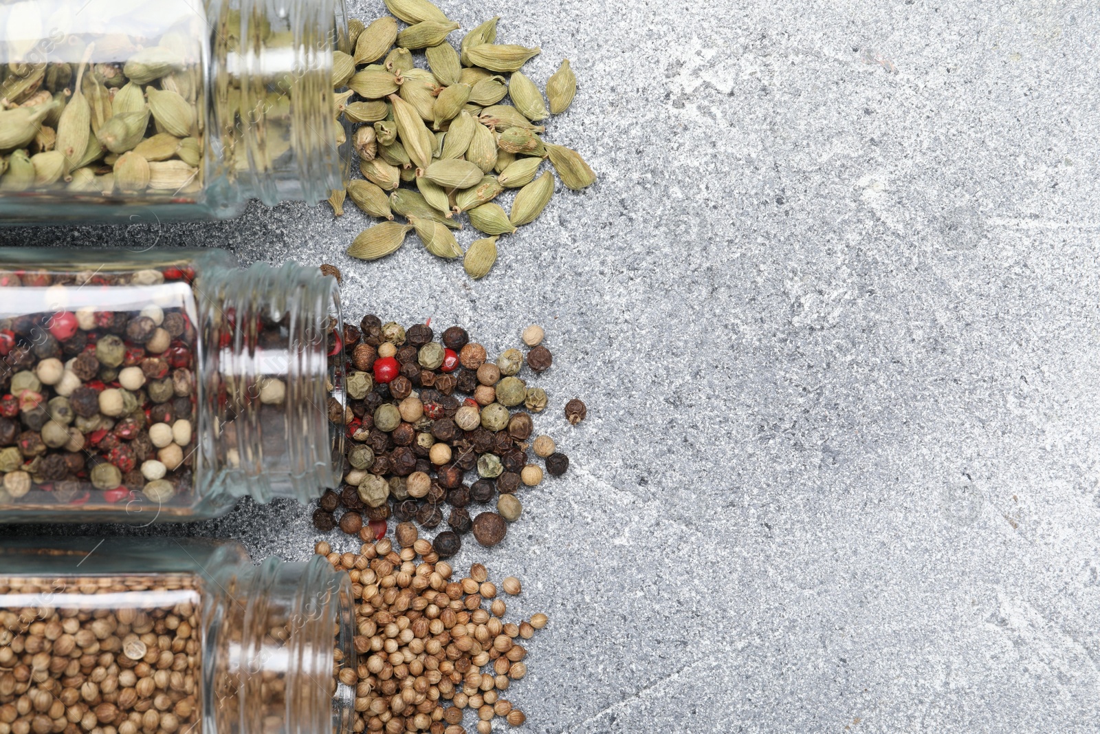 Photo of Different spices in glass jars on grey table, top view. Space for text