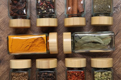 Photo of Different spices in glass jars on wooden table, flat lay