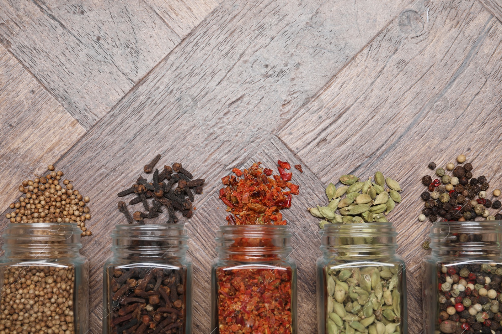 Photo of Different spices in glass jars on wooden table, flat lay. Space for text