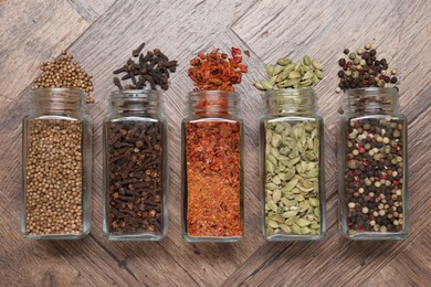 Different spices in glass jars on wooden table, flat lay