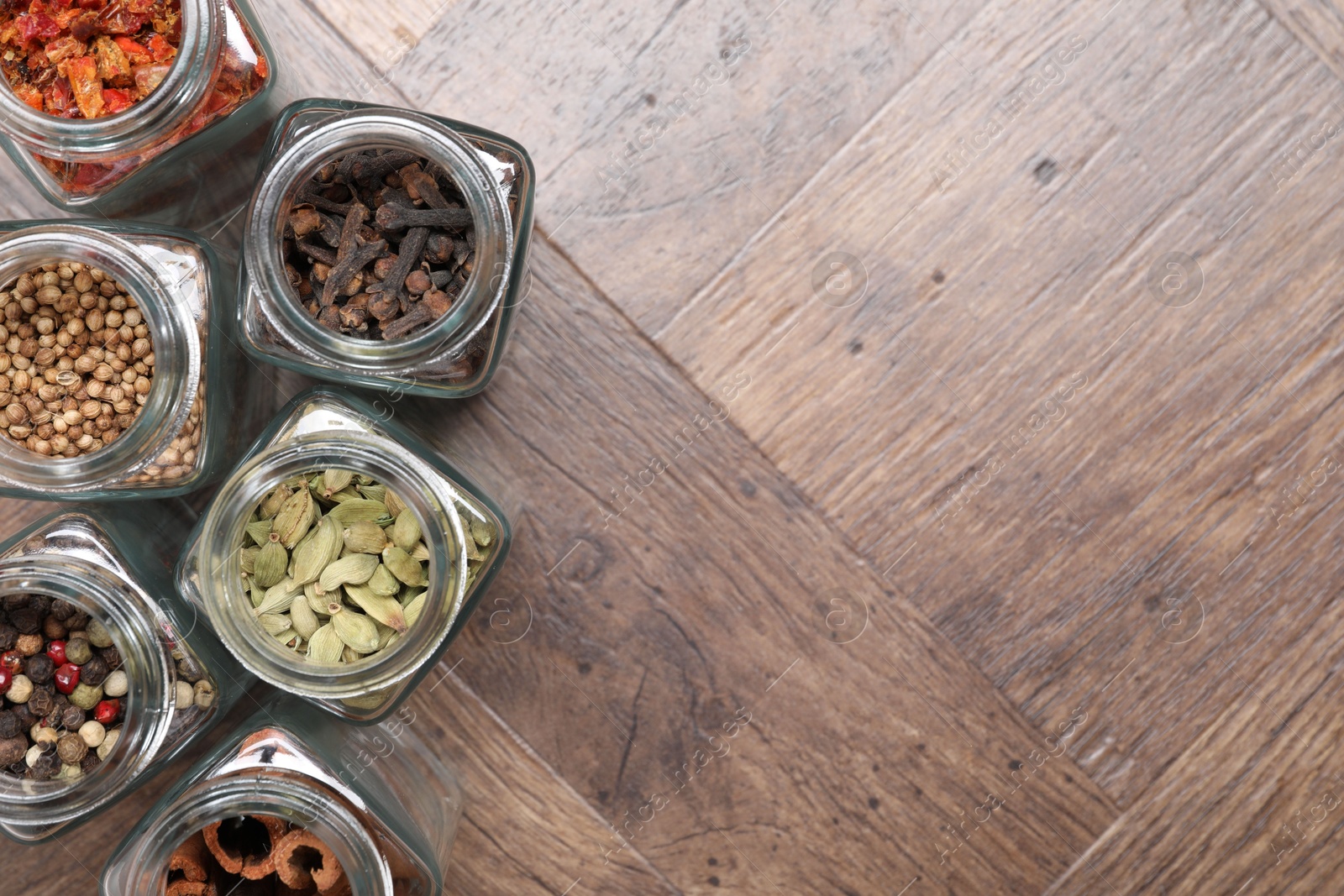 Photo of Different spices in glass jars on wooden table, flat lay. Space for text