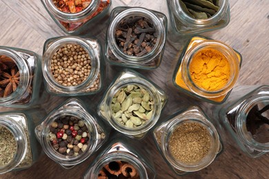 Different spices in glass jars on wooden table, flat lay