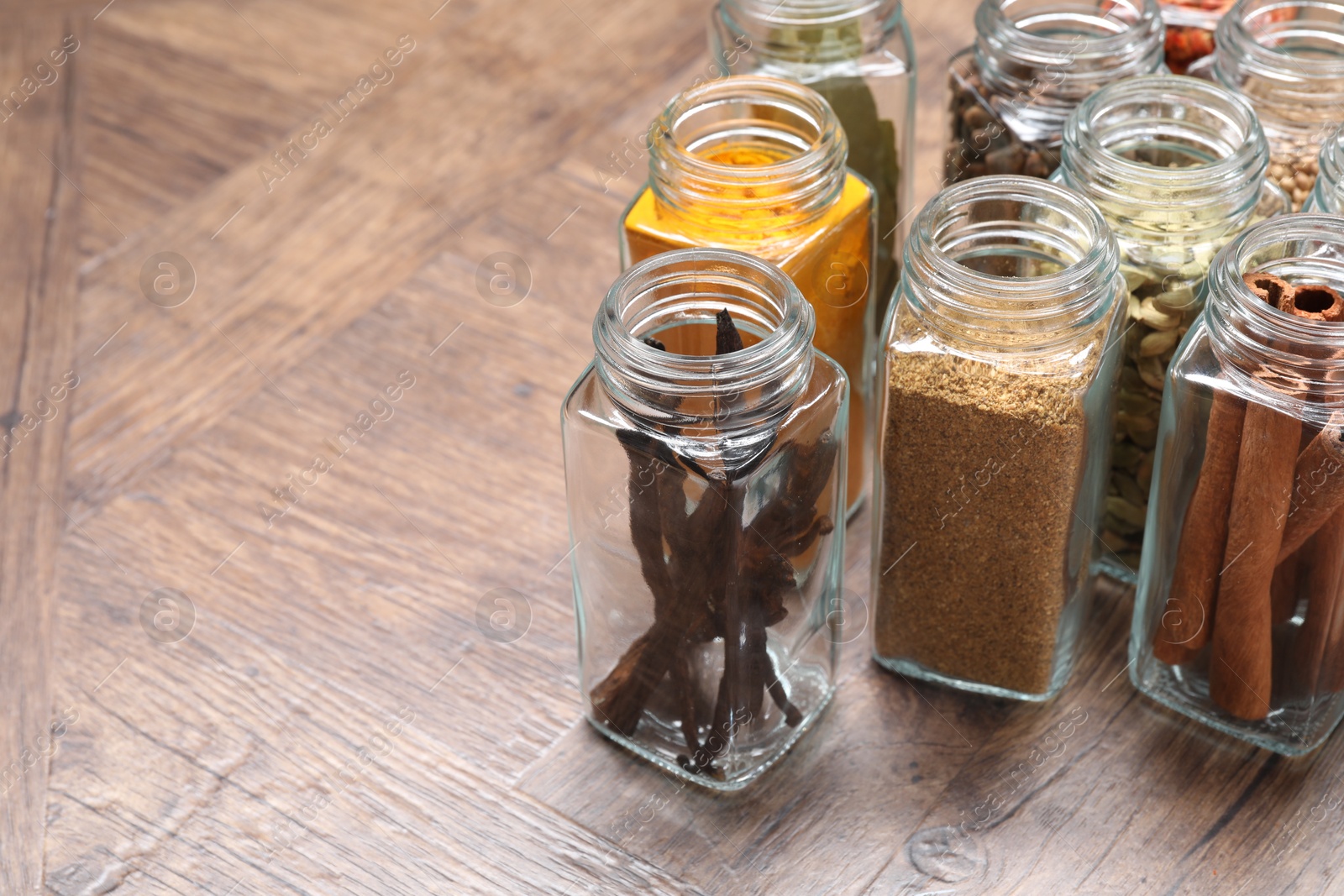 Photo of Different spices in glass jars on wooden table, space for text