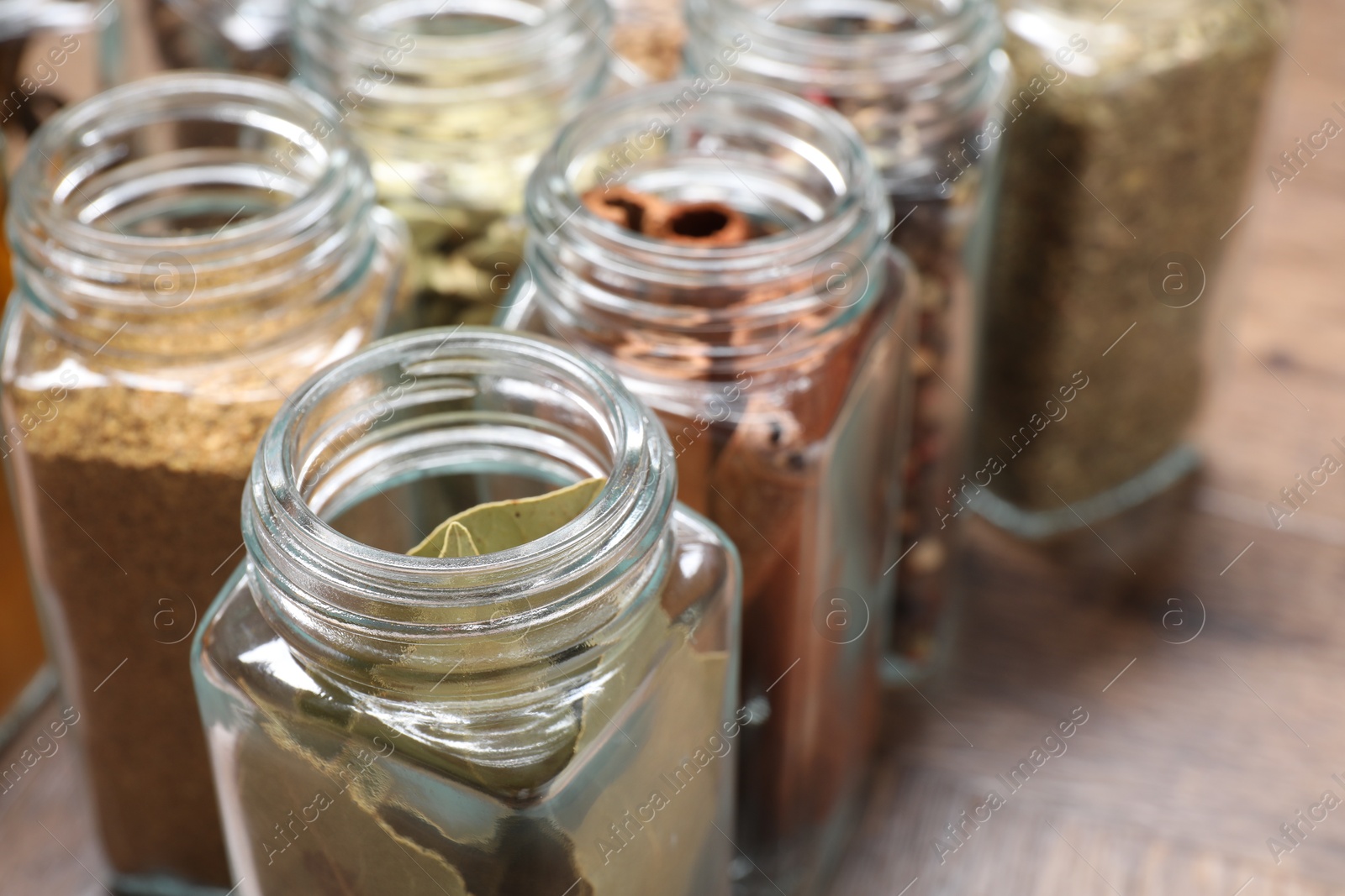 Photo of Different spices in glass jars on wooden table, closeup