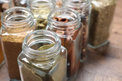 Different spices in glass jars on wooden table, closeup