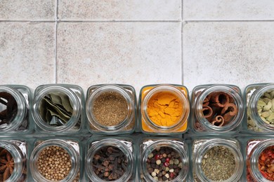 Photo of Different spices in glass jars on light tiled table, top view. Space for text