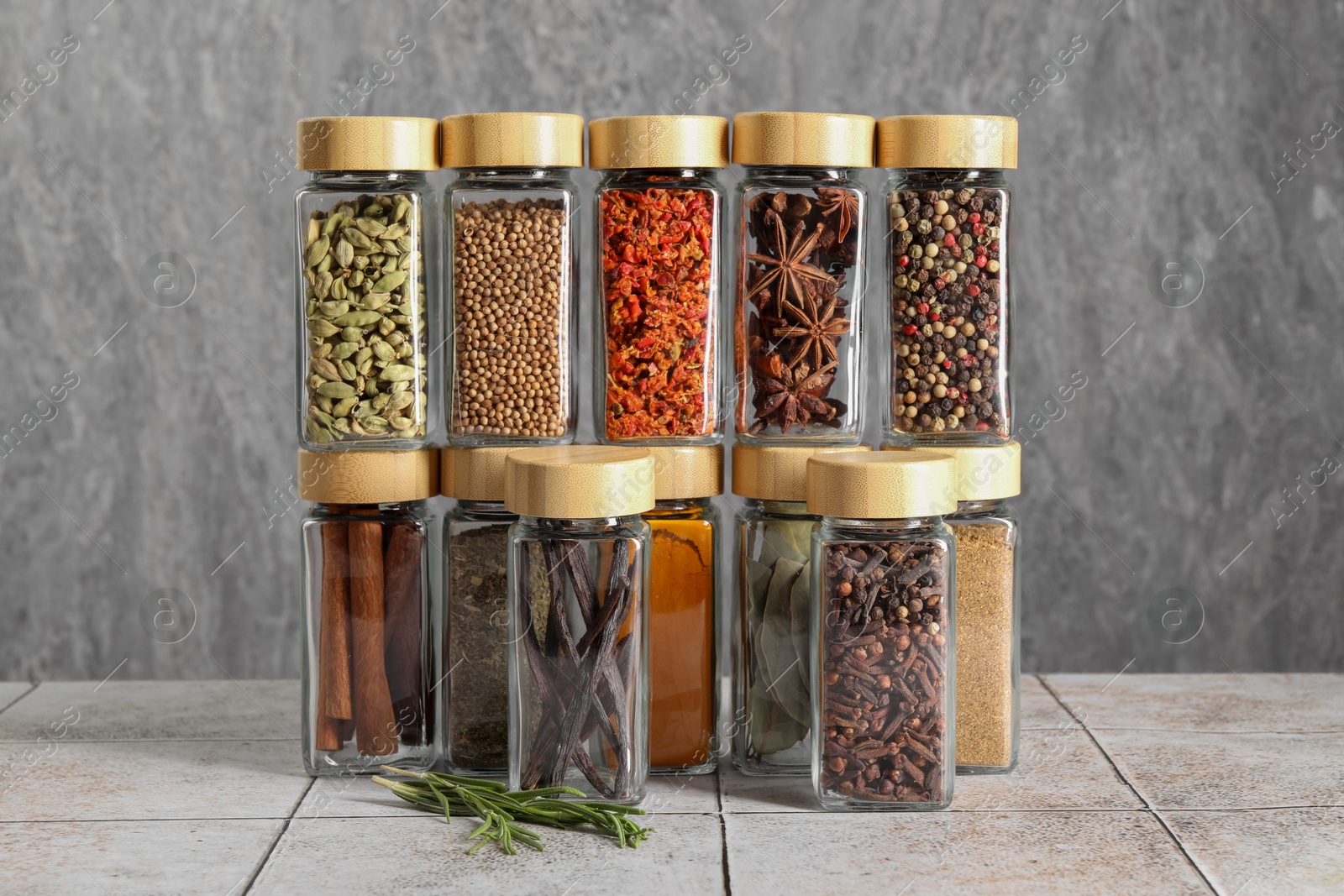 Photo of Different spices in glass jars on light tiled table