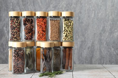 Different spices in glass jars on light tiled table