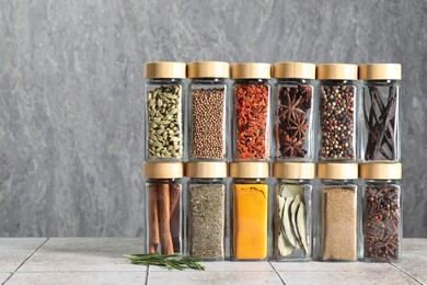 Photo of Different spices in glass jars on light tiled table, space for text