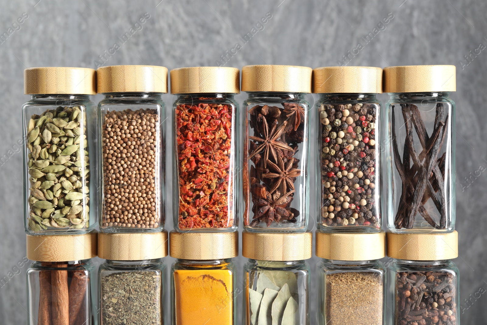 Photo of Different spices in glass jars against grey wall