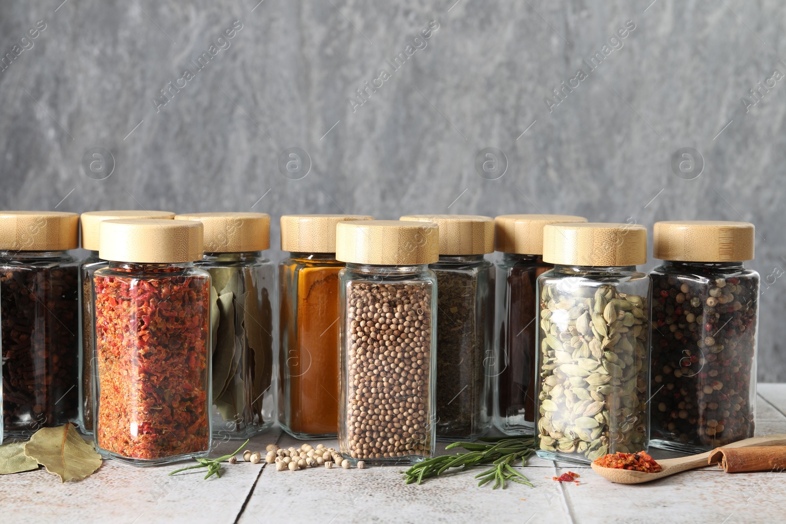 Photo of Different spices in glass jars on light tiled table