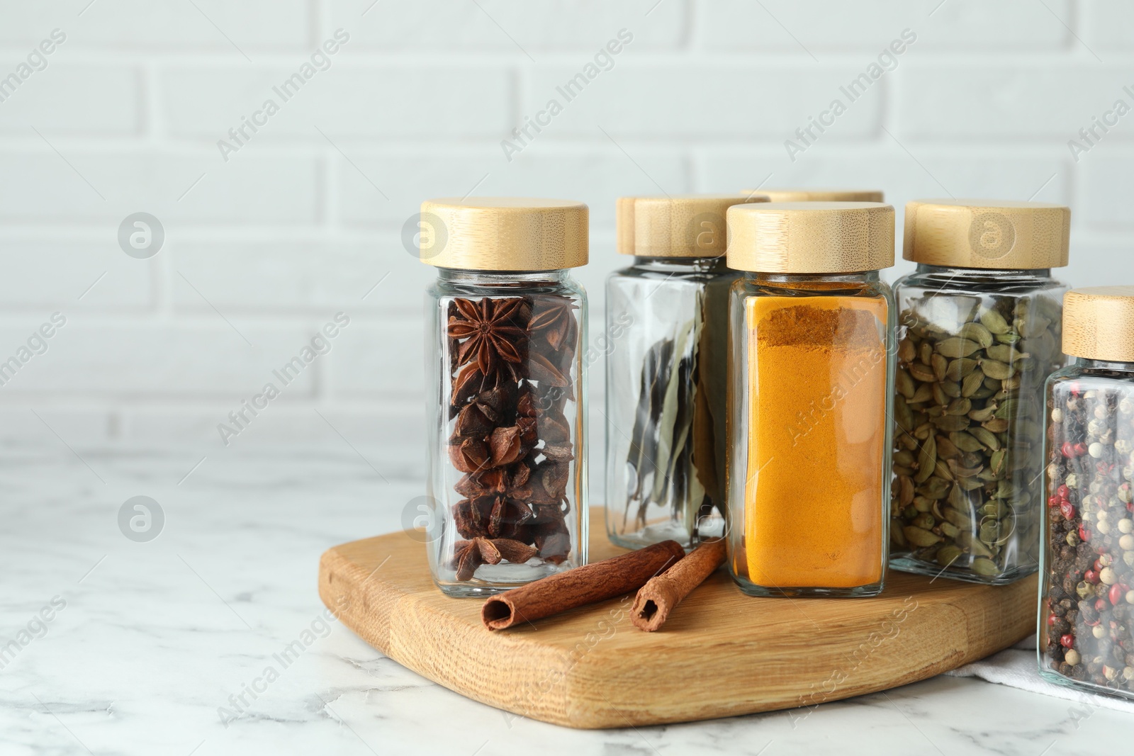 Photo of Different spices in glass jars on white marble table, space for text