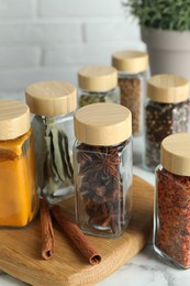 Different spices in glass jars on white marble table