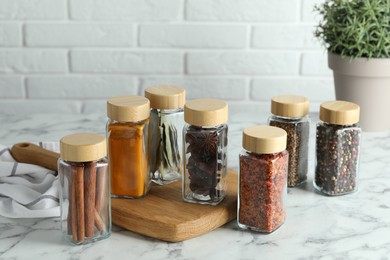 Different spices in glass jars on white marble table