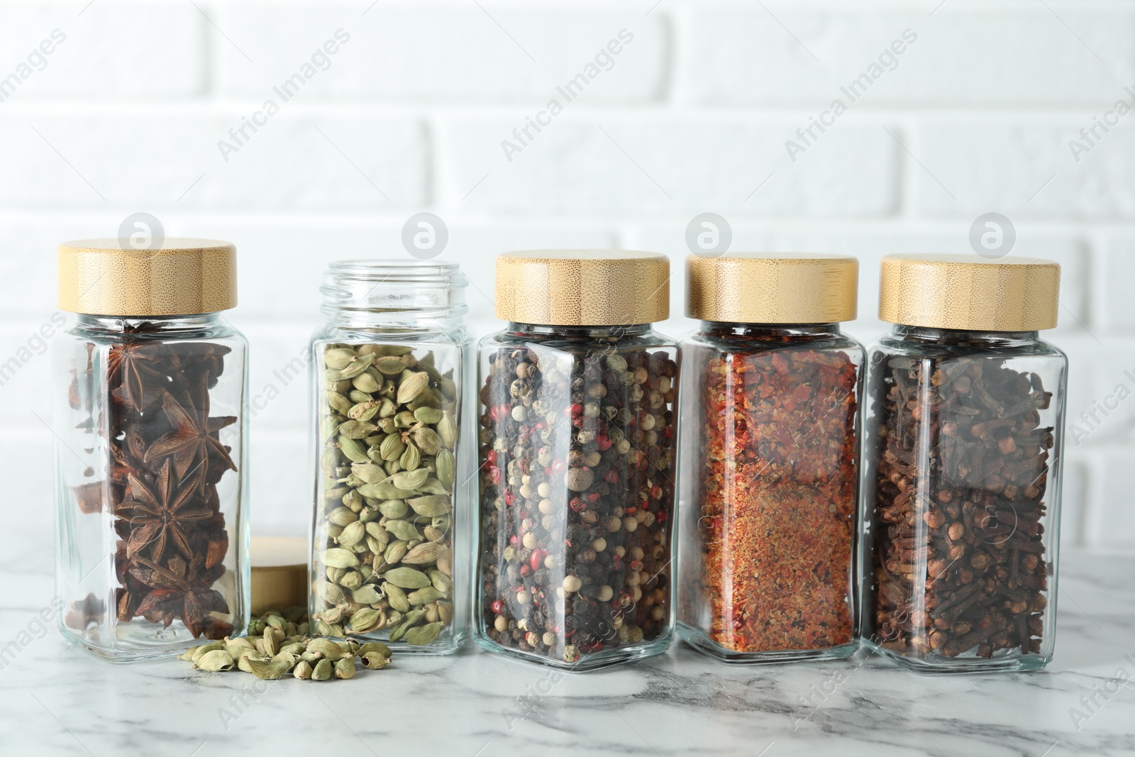 Photo of Different spices in glass jars on white marble table