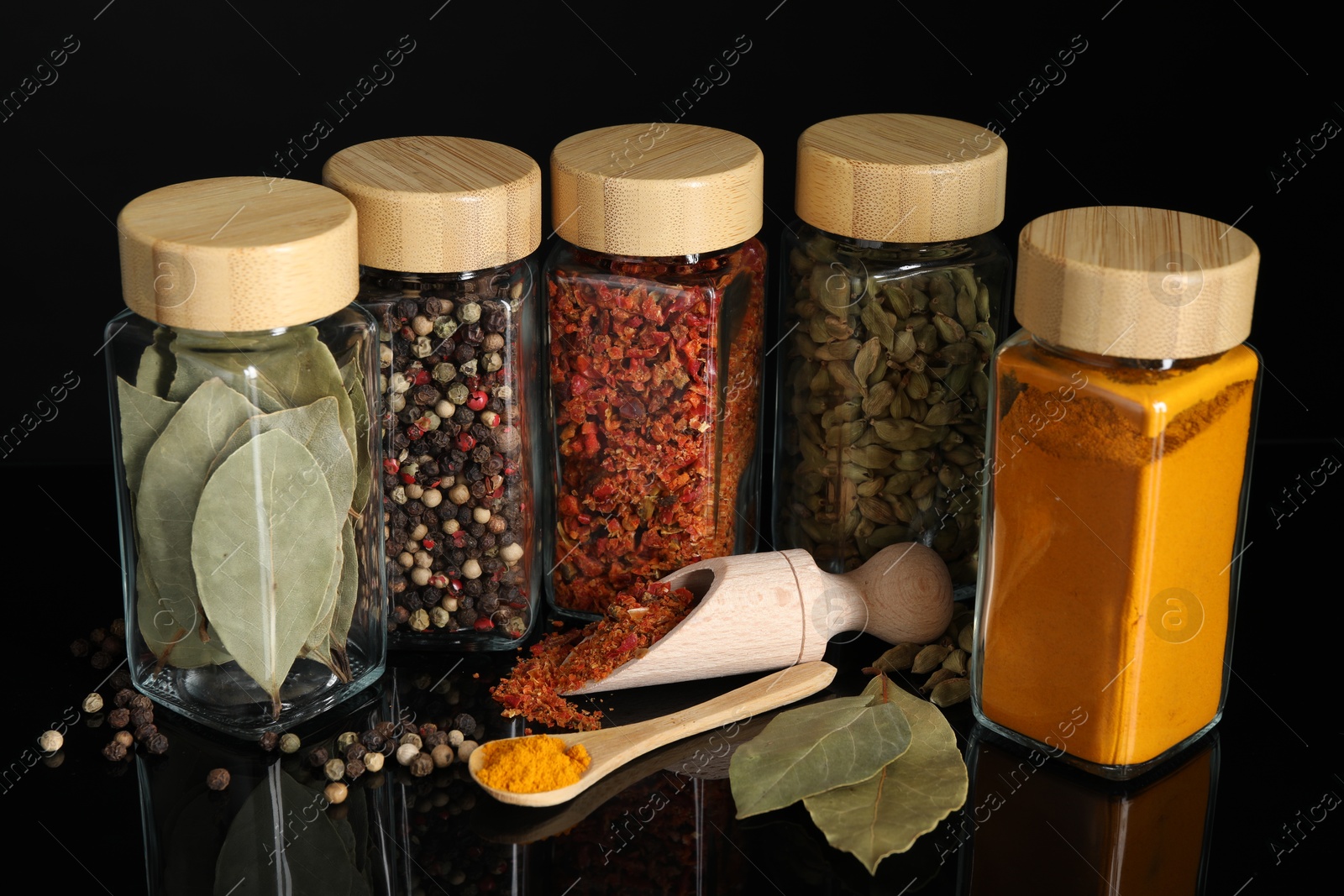 Photo of Different spices in glass jars on black mirror surface