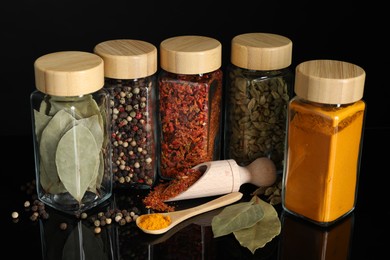 Photo of Different spices in glass jars on black mirror surface