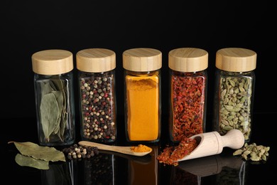 Photo of Different spices in glass jars on black mirror surface