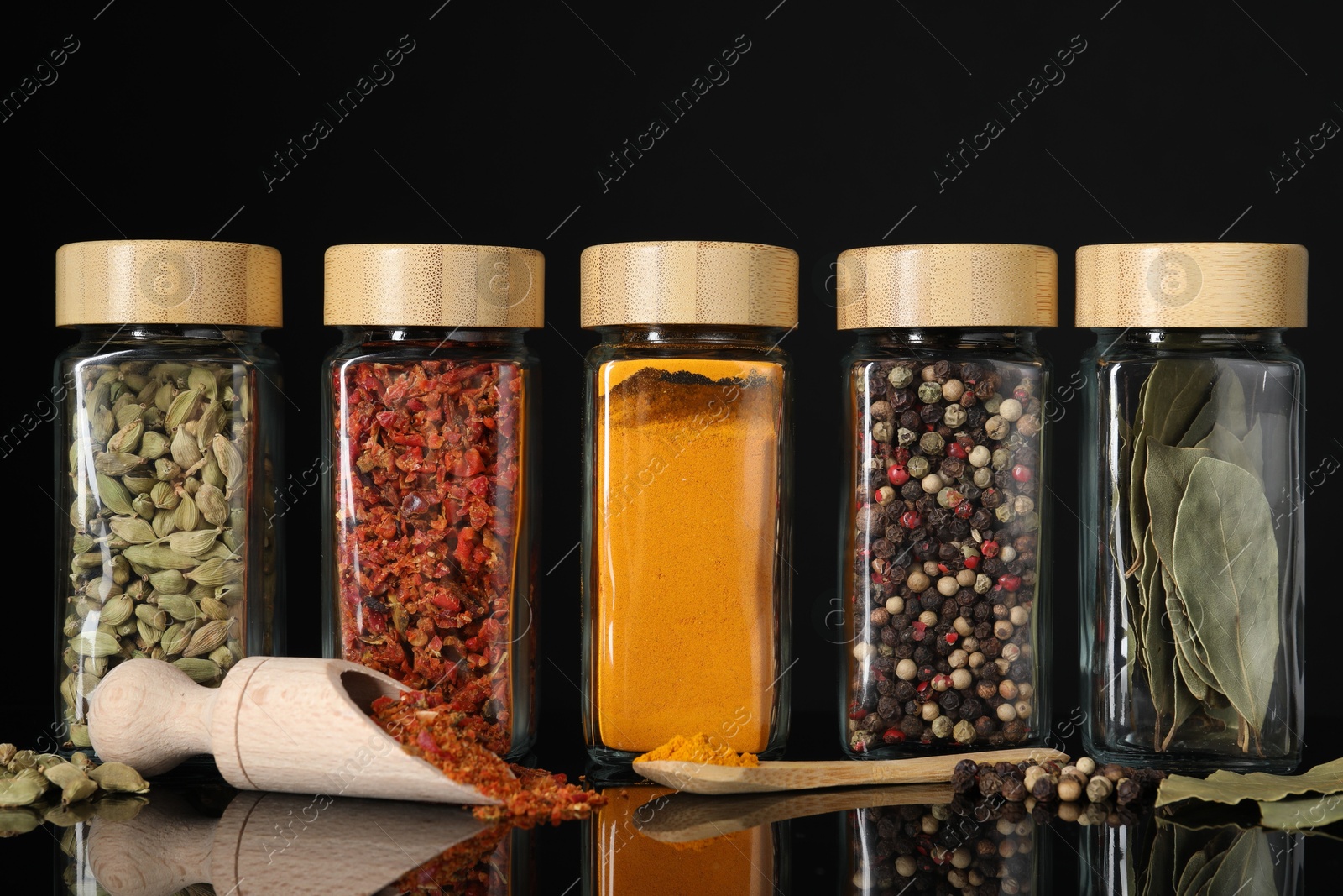 Photo of Different spices in glass jars on black mirror surface