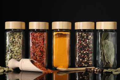 Different spices in glass jars on black mirror surface