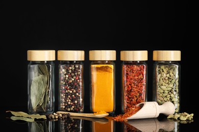 Different spices in glass jars on black mirror surface