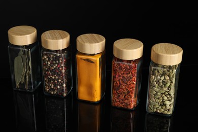 Different spices in glass jars on black mirror surface