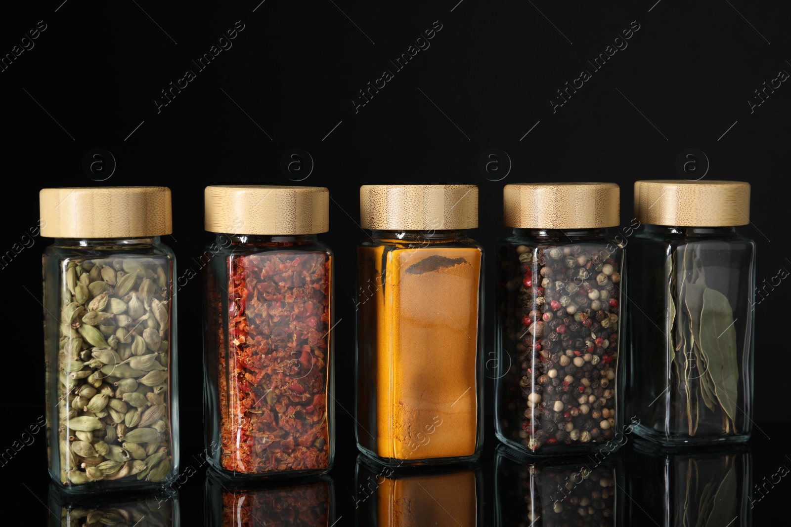 Photo of Different spices in glass jars on black mirror surface