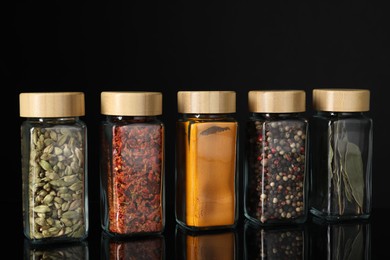 Different spices in glass jars on black mirror surface