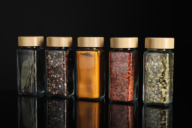 Photo of Different spices in glass jars on black mirror surface