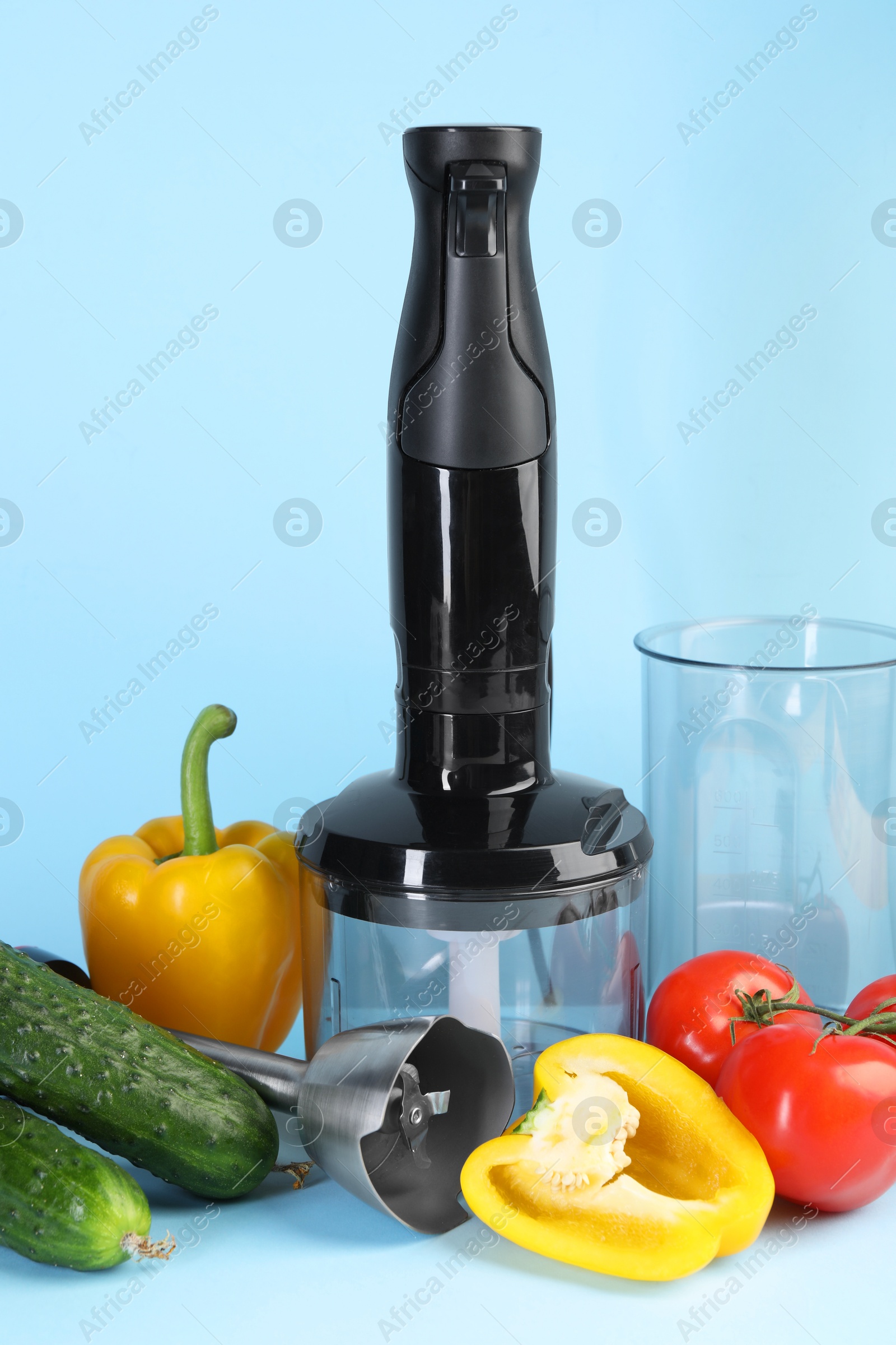 Photo of Hand blender kit and fresh vegetables on light blue background