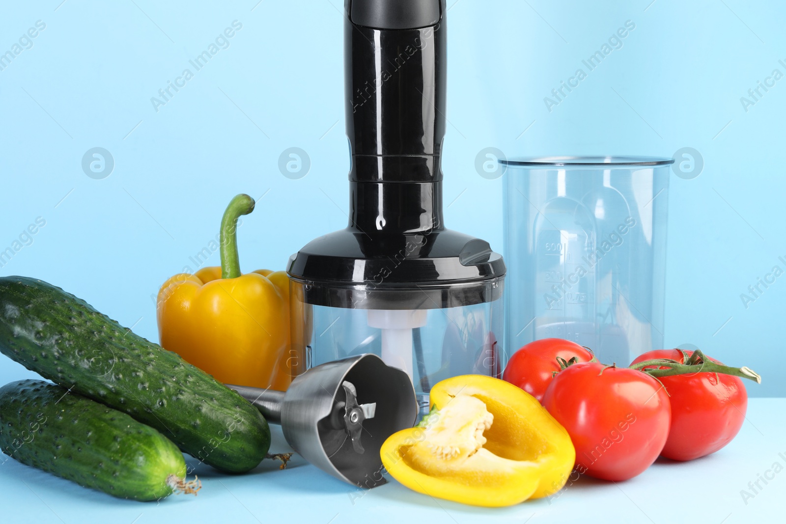 Photo of Hand blender kit and fresh vegetables on light blue background, closeup