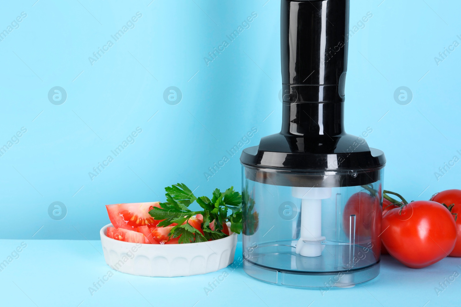 Photo of Hand blender kit, fresh tomatoes and parsley on light blue background, space for text