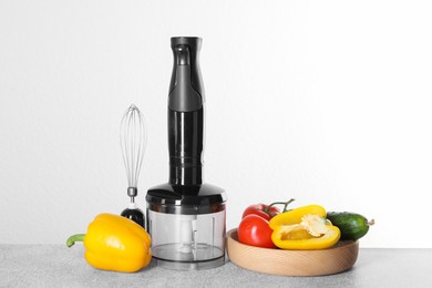 Hand blender kit and fresh vegetables on gray table against white background