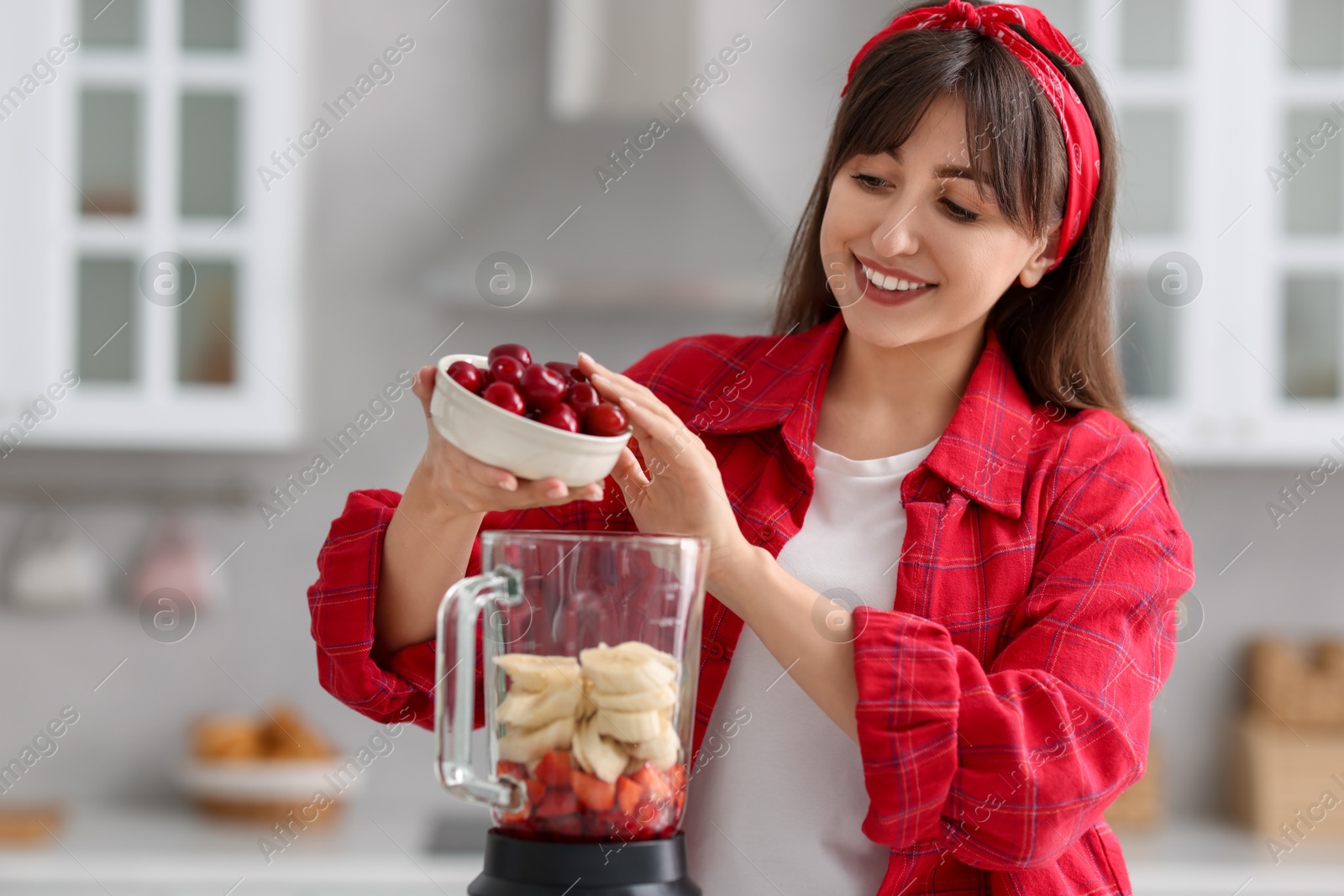 Photo of Young woman making delicious smoothie with blender in kitchen
