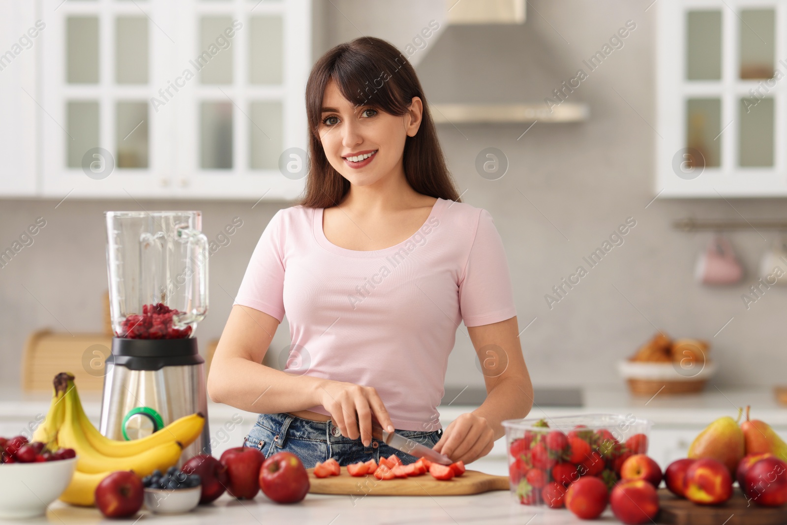 Photo of Young woman making delicious smoothie with blender at white marble table in kitchen