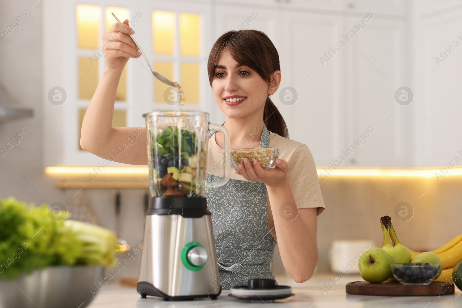 Photo of Young woman making delicious smoothie with blender at white marble table in kitchen