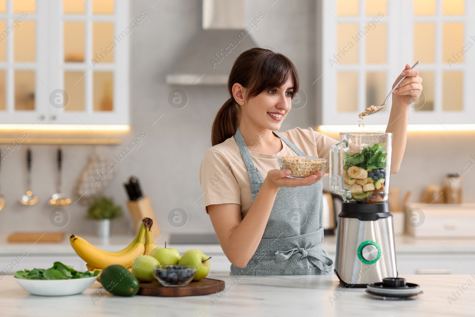 Photo of Young woman making delicious smoothie with blender at white marble table in kitchen